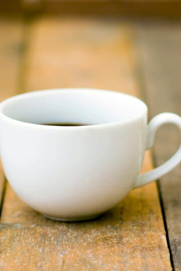 Prosta biała filiżanka kawy na rustykalnym drewnianym stole, idealna na przytulny poranek. Obraz nawiązujący do tytułu "stres w wersji instant"